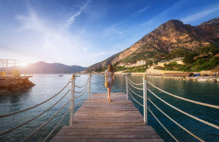 Young woman on wooden pier on sea shore is looking on mountainの写真素材