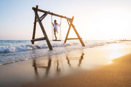 Happy young woman on wooden swing in water, beautiful blue seaの写真素材