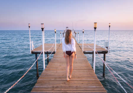Happy young woman in bikini walking on wooden pier on the seaの写真素材