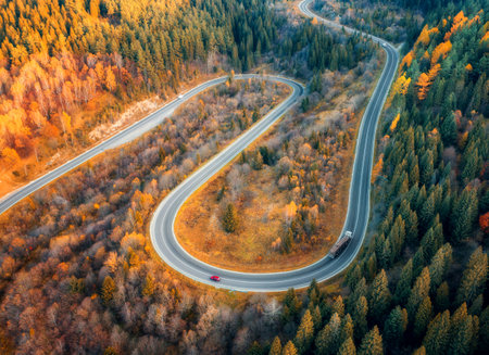 Aerial view of winding road with car in colorful autumn forestの写真素材