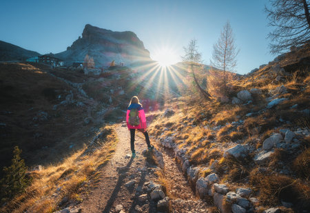 Walking girl with backpack on the trail in mountains at sunsetの写真素材