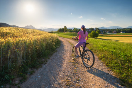 Woman on mountain bike on gravel road at sunset in summerの写真素材