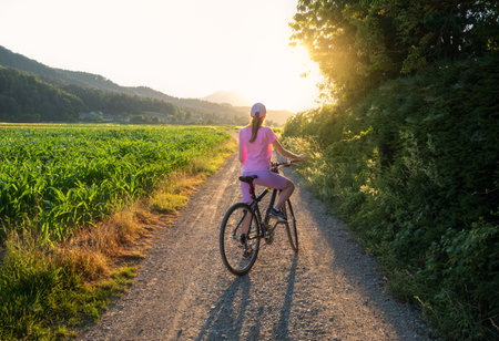 Woman on mountain bike on gravel road at sunset in summerの写真素材
