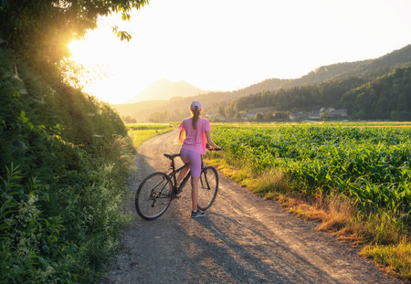 Woman on mountain bike on gravel road at sunset in summerの写真素材