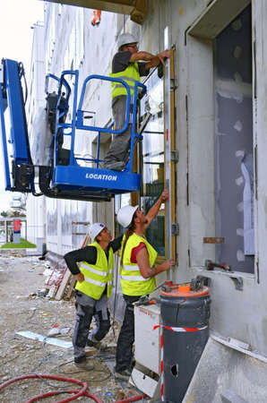Besançon, France - August 27, 2014: Construction workmen on the ground and on a cherry picker installing windows on a construction site.のeditorial素材
