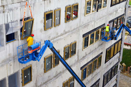 Besançon, France - November 3, 2014: Construction workmen on cherry pickers installing windows on a construction site.のeditorial素材