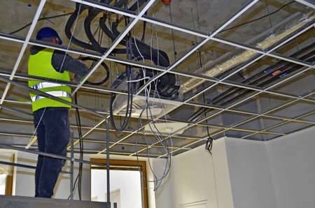 Besançon, France - April 9, 2015: Workman installing wirings under a suspended ceiling on a construction site.のeditorial素材