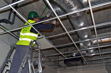 Besançon, France - February 16, 2015: Workman installing ductworks under a suspended ceiling on a construction site.のeditorial素材
