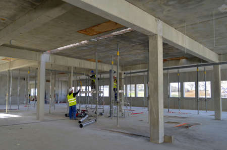 Besançon, France - March 18, 2014: Workmen installing ductwork among struts in an empty room on a construction site.のeditorial素材