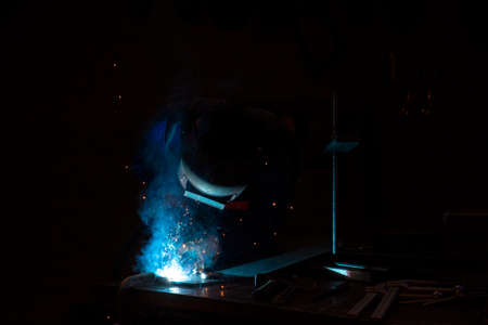 Welder welding metal in workshop with sparks. Welding steel on site at a engineering site. The sparks from the arc light the welding shield helmet.の写真素材