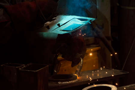 Industrial welder with torch and protective helmet in big hall welding metal profiles.