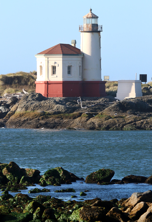 Lighthouse on coastline of blue water and rocky shore during mid morning sun.の写真素材