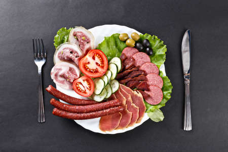 meat, hamon, sausage slices assortment on plate with spoon and knifeの写真素材