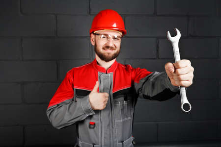 man wearing overalls with red helmet and wrench near brick wallの写真素材