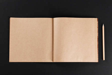 Open blank notepad with empty craft pages with a pencil on black backgroundの写真素材
