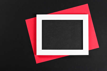 horizontal white photo frame with black field and red paper under angle on black background isolated with real shadowsの写真素材