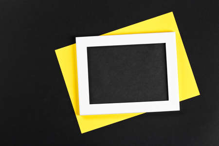 horizontal white photo frame with black field and yellow paper under angle on black background...