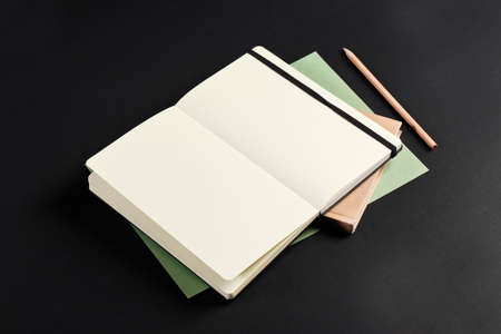 Open blank notepad with empty white pages laying above book with pencil on black background. ideal for textの写真素材