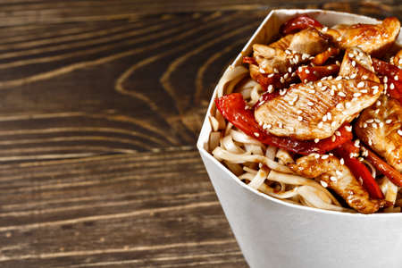 Delicious wok noodles box container with udon and chicken on wooden table. Chinese and asian takeaway fast food.の写真素材