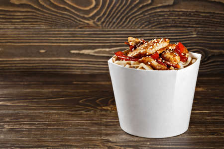 Delicious wok noodles box container with udon and chicken on wooden table. Chinese and asian takeaway fast food.の写真素材