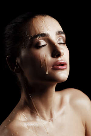 Beauty Portrait of Young Woman with Strobing Makeup Liquid on Face. Wet Body Effect. Strobing Highlighting technique. Professional Retouch. Studio Photo. Ideal commercial concept. Black backgroundの写真素材
