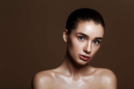 Strobing or Highlighting makeup. Closeup portrait of beautiful girl with strobing highlighter powder. Nice Glow. Perfect retouch. Studio photo beige background. Wet body effectの写真素材