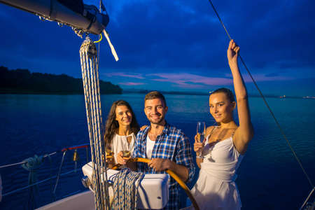 Night walk on a yacht. Young people is resting on a yacht. Boy and girls drinking champagne on a yacht.の写真素材