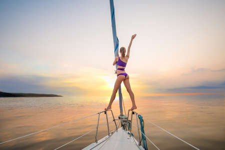 Girl sailing  on the yacht on a meeting the sun. Girl waves her hand from the yacht. Romantic walk on the yacht. Traveling on a yacht.の写真素材