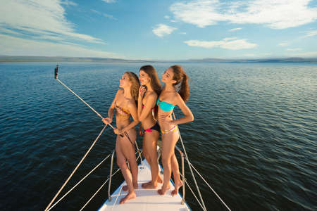 Girlfriends rest on a yacht in the middle of the ocean. Beautiful girl at the resort. Girls do selfie on a yacht. Weekend on a yacht. Cruise on a yacht at sea.の写真素材