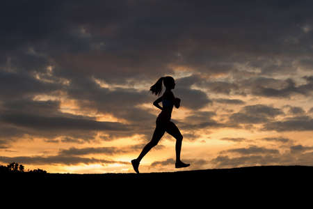 Morning jogging  the girl on the background of a beautiful sky. Girl running on the evening park. Running on fresh air. Healthy sport.の写真素材