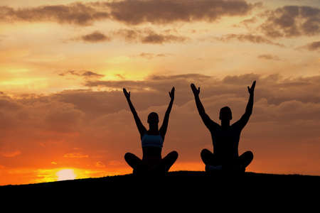 Boy and girl engage in yoga on the nature. A man and a woman meditating in the mountains. People relax at sunset.の写真素材