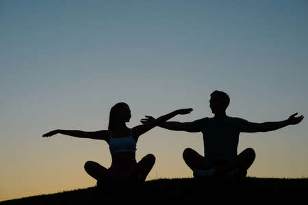 Boy and girl waving their hands at sunset. Silhouette figures of people at sunset. People relax. Rest at nature.の写真素材