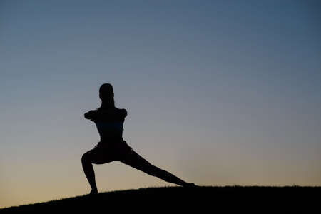 Silhouette of the the sportswoman on the background of sunset. Girl doing exercise on the nature. Warm up outdoors. Fitrnes on the nature in the mountains.の写真素材