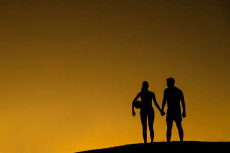 Loving couple of volleyball players. Guy and girl walk on sunset background. Love story. Silhouette of loving couple on the background of a beautiful sky.の写真素材