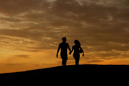 Loving couple of sportsmen walk on the evening hills. Silhouette of loving couple. Evening walk of husband and wife. Family walk.の写真素材