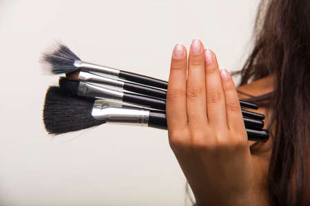 The brunette with long hair is holding makeup brush set. Nice lady is showing cosmetic brush set...