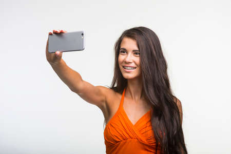 Beautiful girl is holding camera and making photo. Young lady is having fun on white background.