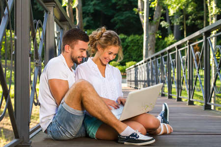 Couple using laptop outdoors.Family in nature have fun with the computer.Young couple using their laptop together.Couple plan a vacation trip route.の写真素材