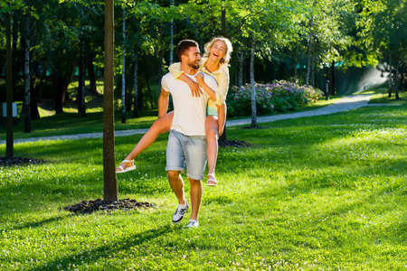 Playing in the park. Lovers enjoying a date. Romantic games. Guy bears the girl on the back.の写真素材