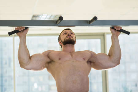 Athlete doing pull-ups. Muscular man in gym. Bodybuilder doing sports. Strong man with muscular arms...
