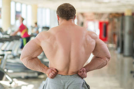 Muscular man's back. Bodybuilder showing his muscular back. People working out in gym on the background.の写真素材
