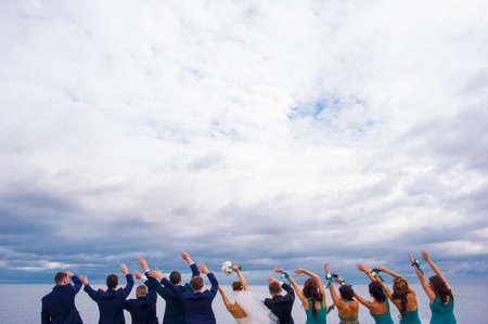 Guests on the wedding celebration are standing on the river pier, holding their hands up and looking in to the distance.の写真素材