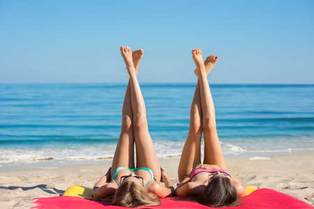 Girls sunbathing on the sea. Girlfriends have a rest on the beach. Long legs of young girls on the beach. Relax on vacation. Sexual girls lying on the seashore.の写真素材