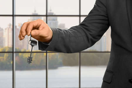 Businessman with key beside window. Adult man holding office key. The new apartment is yours....