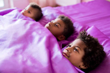 Three black boys in bed. Afro boys on purple bed. Time to go to school. It's breakfast time.