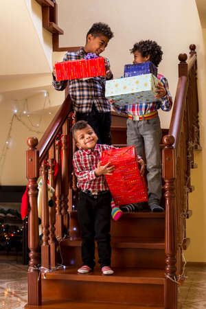 Happy boys with Christmas presents. Children holding presents on stairs. Three happy brothers. Share your joy with relatives.の写真素材