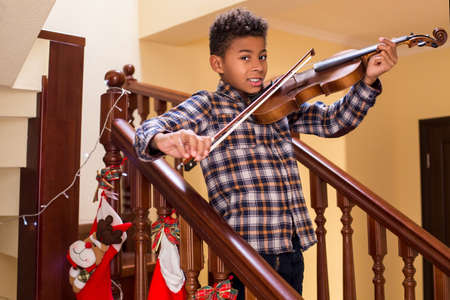 Smiling afro kid plays violin. Boy playing violin on Christmas. Young violinist's smile. True Christmas concert.の写真素材