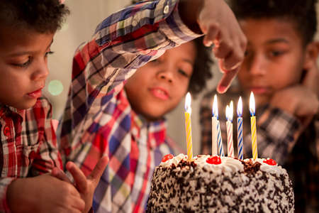 Boy holding finger over candle. Kid playing with cake's candles. Don't burn yourself. Old enough to try this.の写真素材