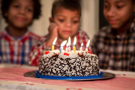 Children watch candles burn out. Boys looking at cake's candles. The youngest brother is sad. So...