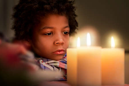 Sad boy looking at candle. Upset boy near Christmas candle. Moment of sadness. Young man's deep emotion.の写真素材